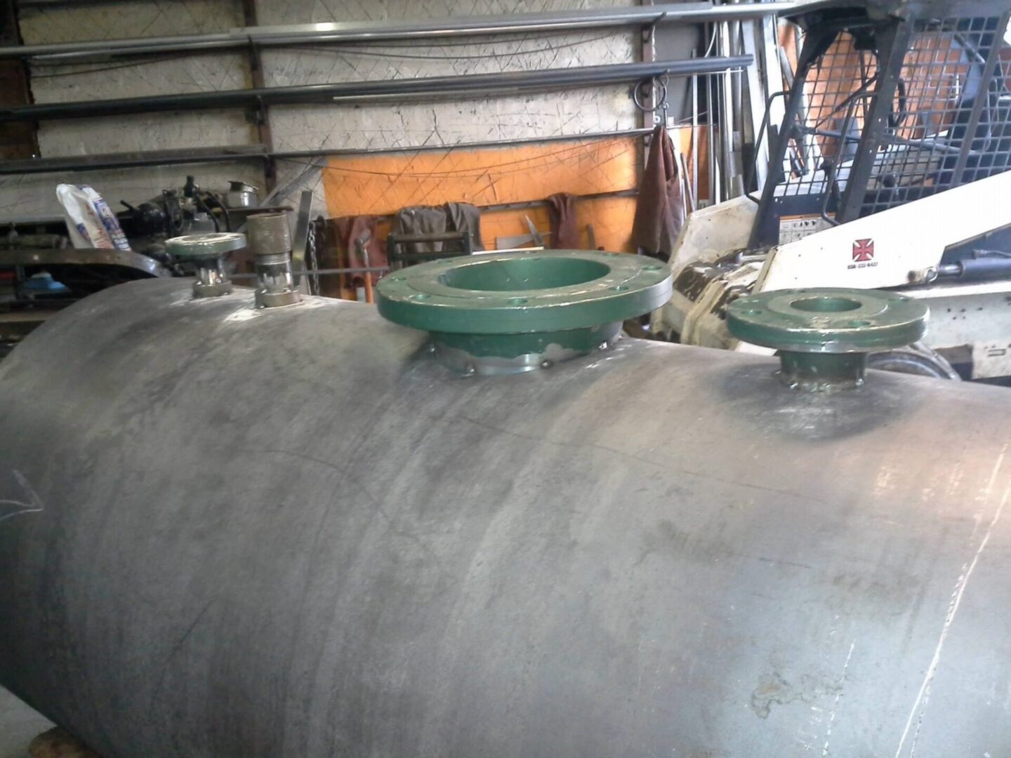 Metal cylindrical tank with green flanges in workshop